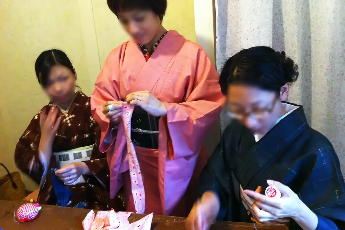 和裁士に運針を教わりながら腰紐を縫う着物姿の参加者