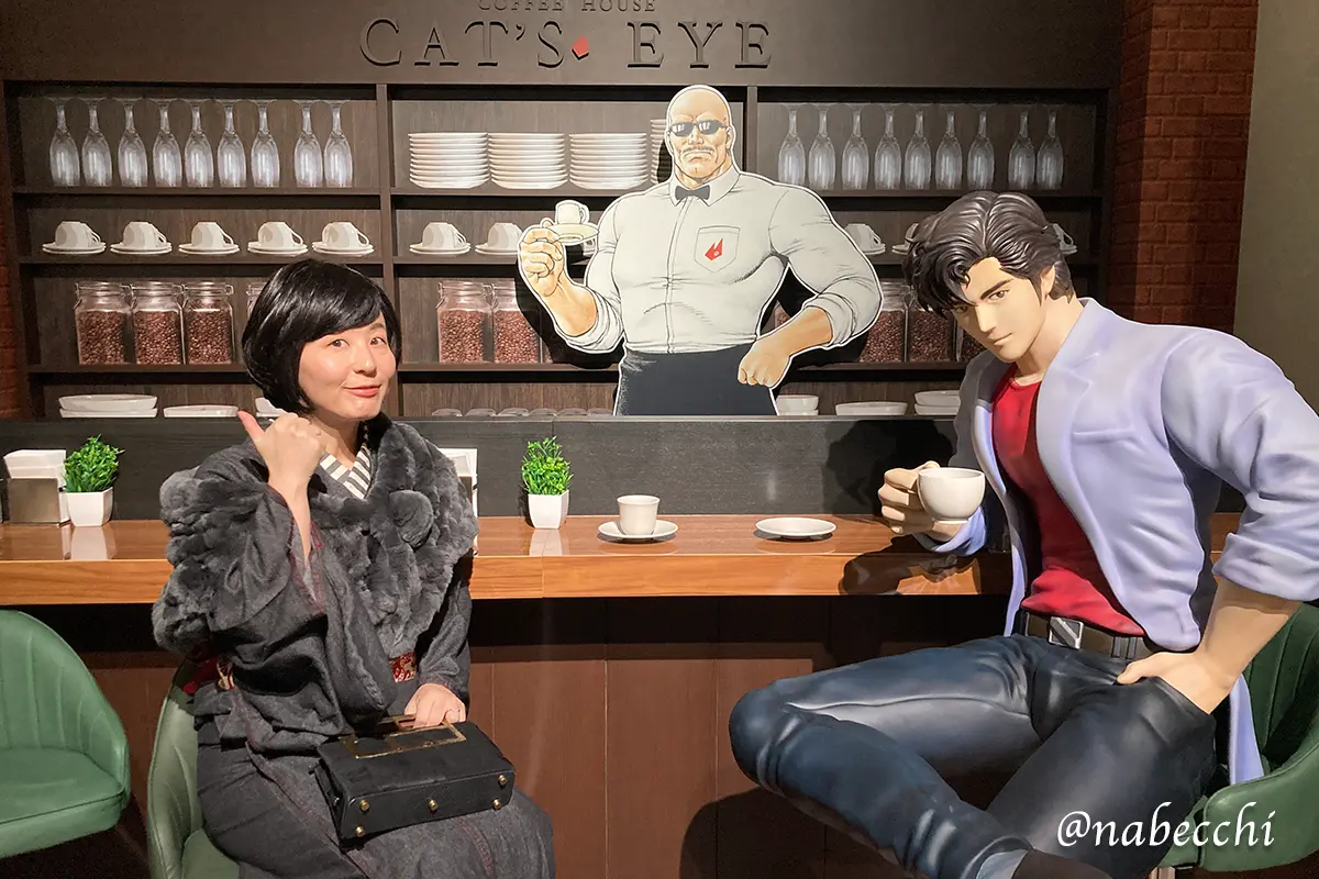 喫茶キャッツアイのセットで、黒デニム着物姿の筆者が冴羽獠と海坊主の等身大パネルと並んで座る3ショット。