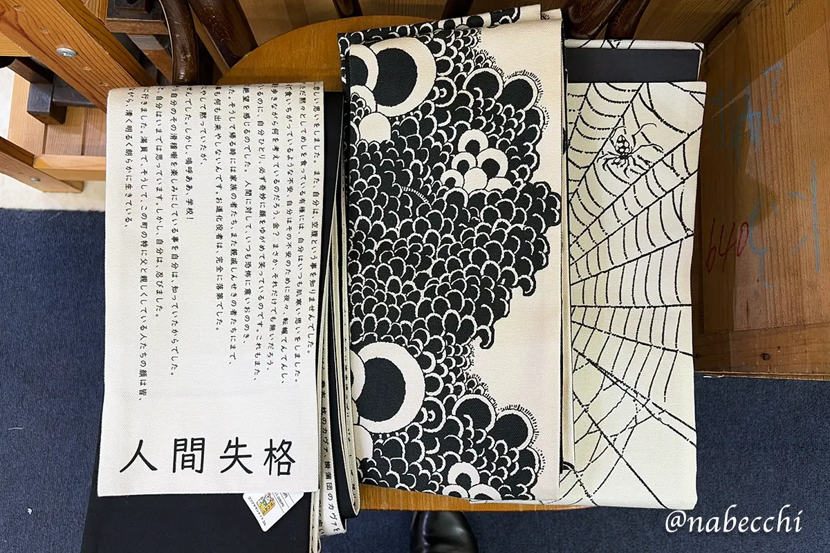 椅子の上に並べられた「人間失格」、ドット、蜘蛛の巣柄の3種類の帯。どれにするか最終選別しているシーン。
