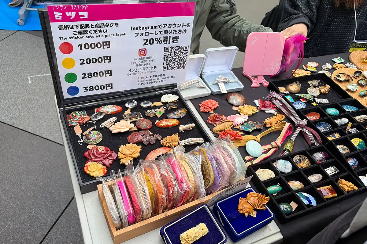 「アンティークきものやミツコ」ブースに並ぶ色とりどりの帯留めと価格表