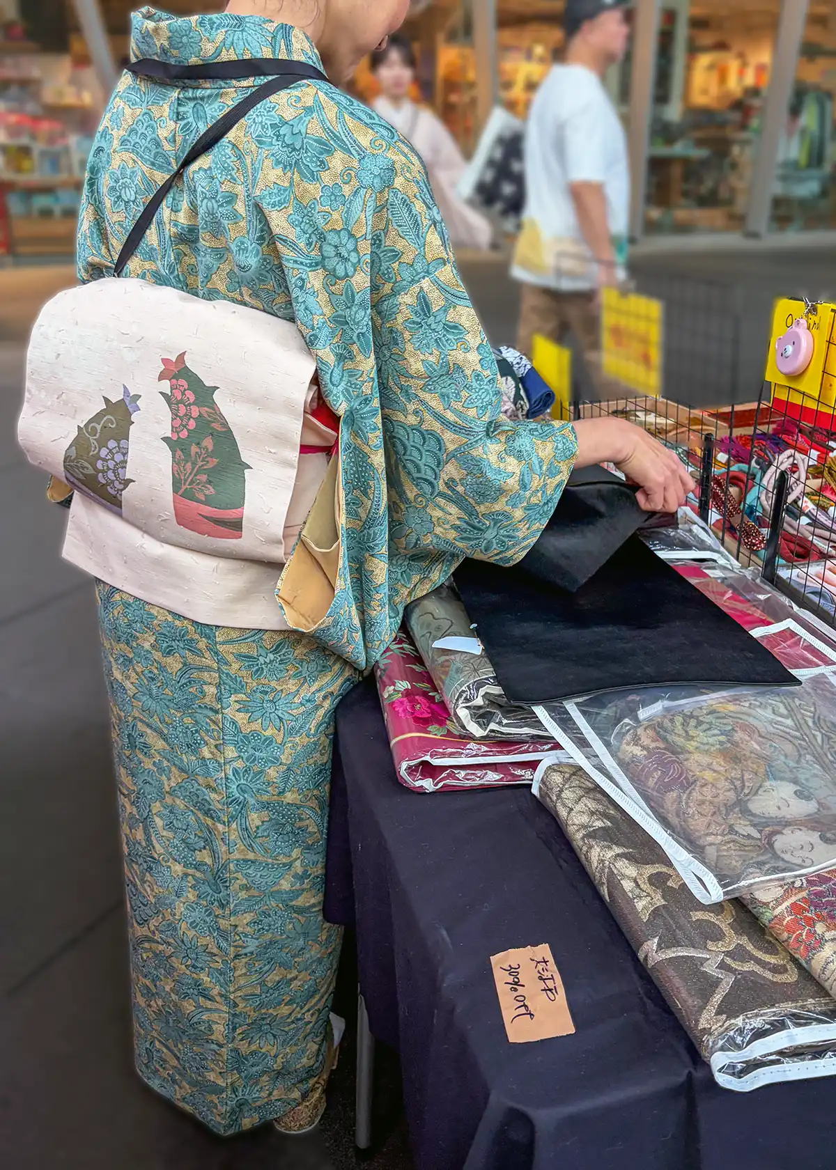たけのこ柄の帯と涼やかな配色の小紋を着こなす「着物の越田」の店員さんの後ろ姿