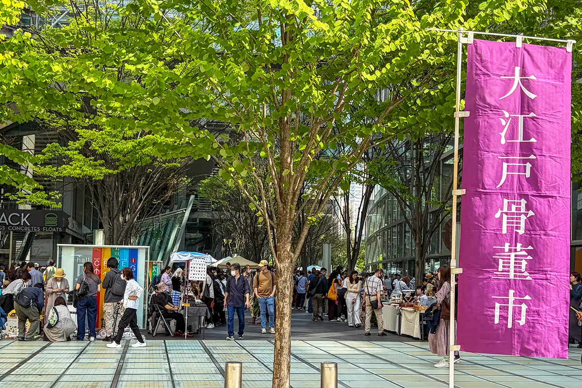 oedo-antique-market-entrance.webp 大江戸骨董市の入り口に立つ紫色の大きなのぼりと鮮やかな新緑の木々