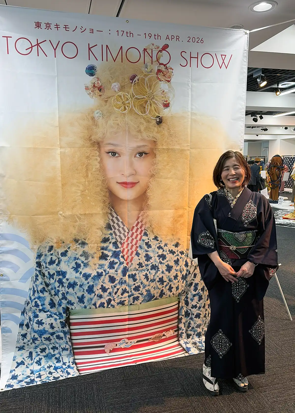 東京キモノショー2026のタペストリー前で記念撮影する筆者の着物コーデ
