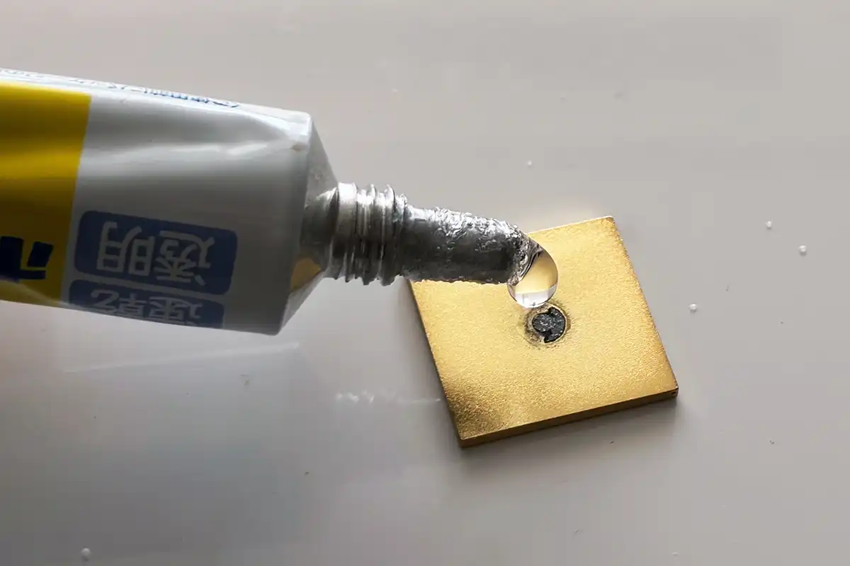 マジョリカタイルのピンバッジ裏面に帯留め金具を接着するためのボンドを塗っている様子