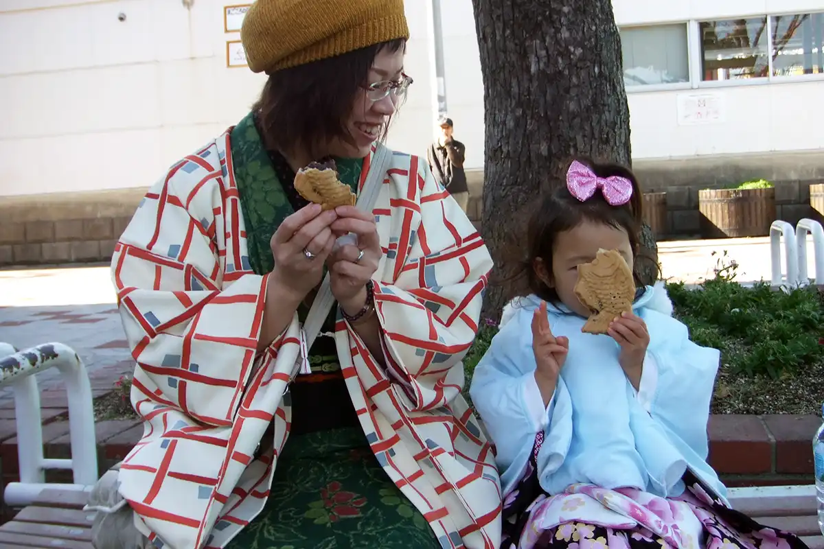 箕面駅前で鯛焼きを食べる着物姿の親子