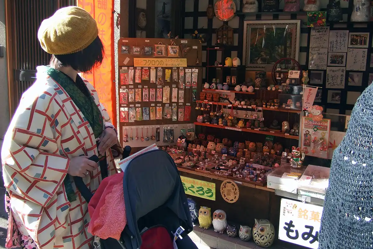 箕面の滝道でフクロウの雑貨が並ぶお土産店を見る着物姿の参加者